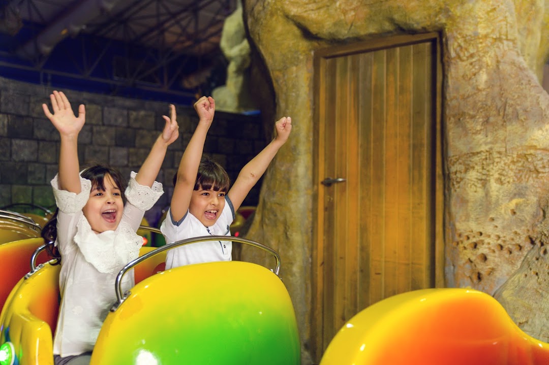 Two excited children with arms raised on a colorful amusement park ride.