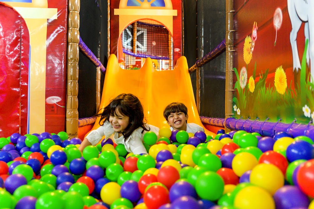 Two happy children playing in a colorful ball pit with a slide.
