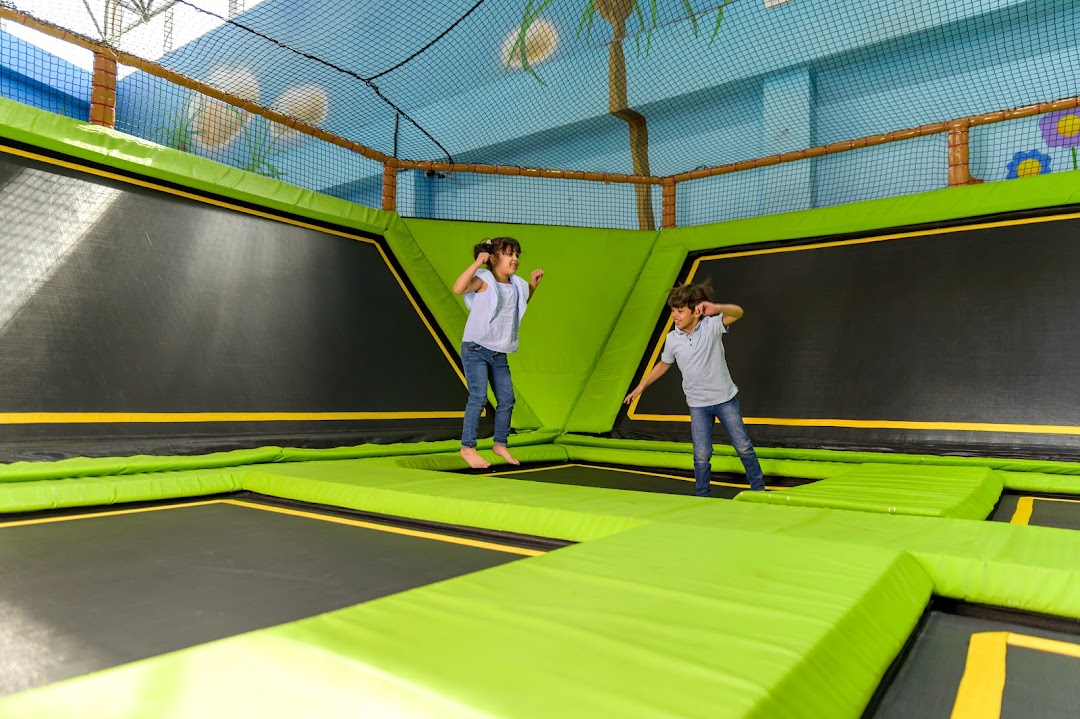 Two children joyfully jumping on a large indoor trampoline park with green padding.