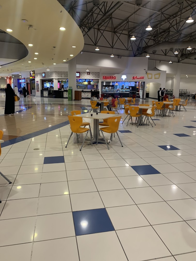 A view of a mall food court with Sbarro and other eateries, featuring seating areas.