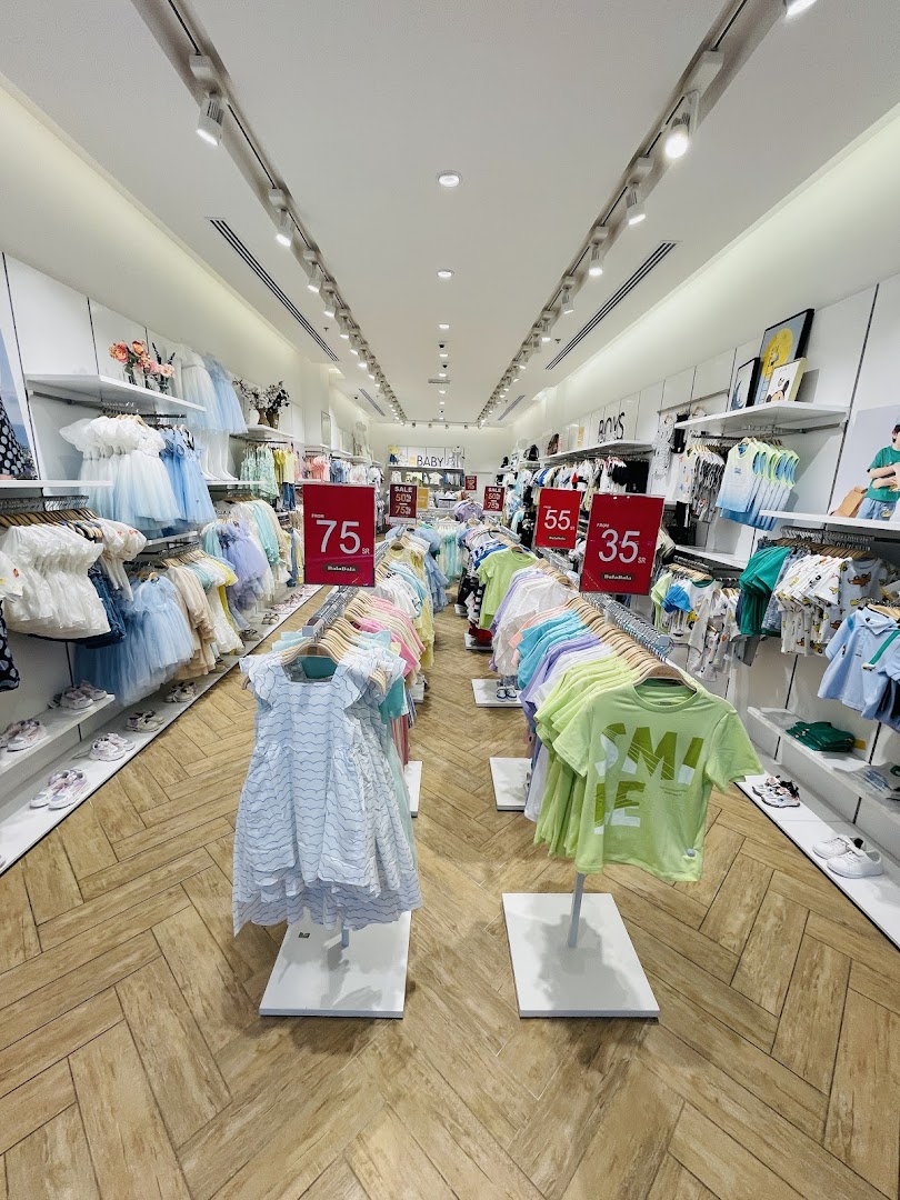 Interior view of a children's clothing store with racks of colorful apparel and sale signs.