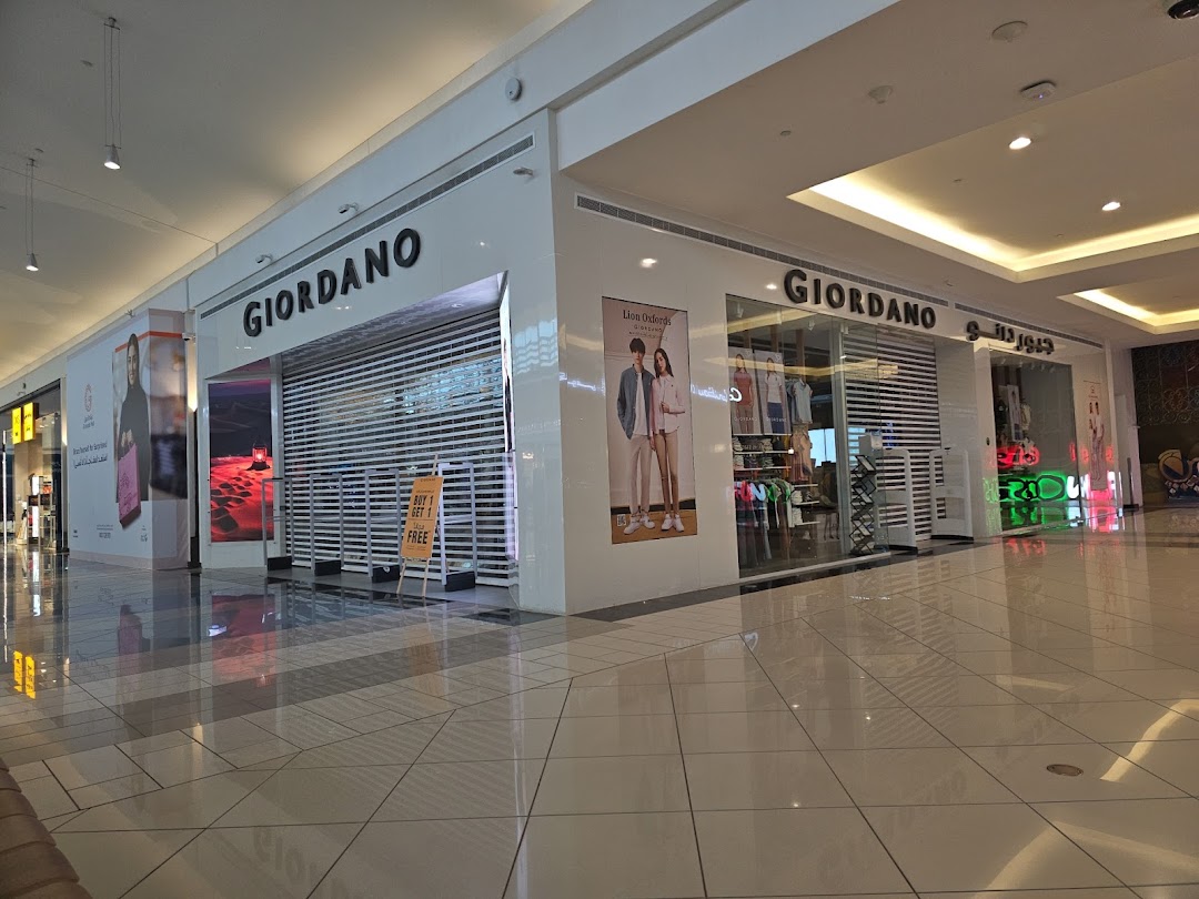 The exterior of a Giordano clothing store in a shopping mall, with its shutters down and a promotional sign.