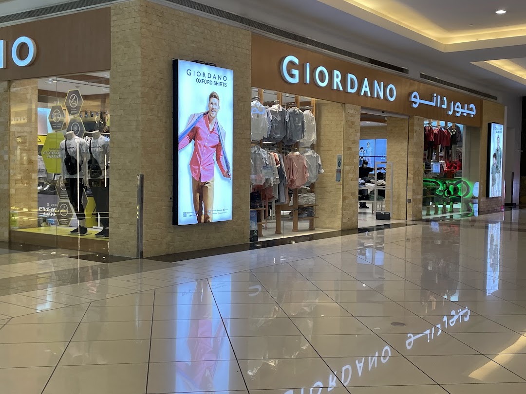 The exterior of a Giordano clothing store with mannequins and displayed shirts.