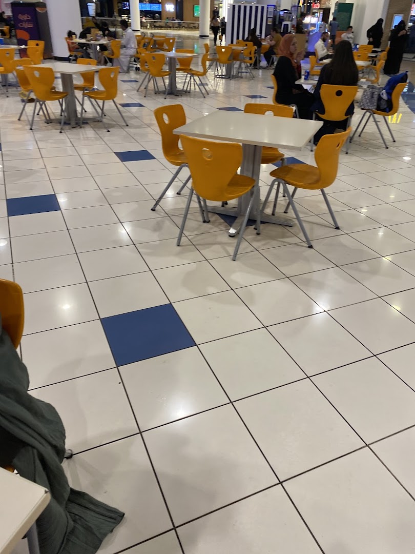 A food court with many tables and chairs, some occupied by diners.