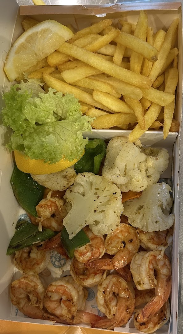 A box of food containing grilled shrimp, french fries, cauliflower, bell peppers, lettuce, and lemon.