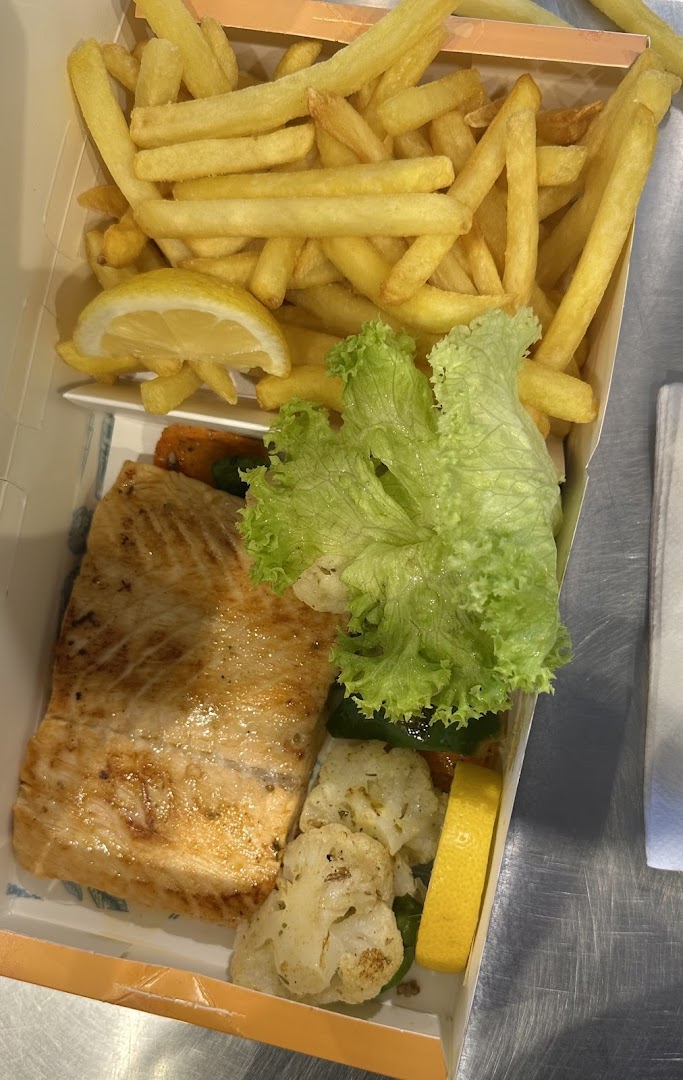 A delicious salmon fillet with fries, salad, and roasted vegetables served in a takeaway box.