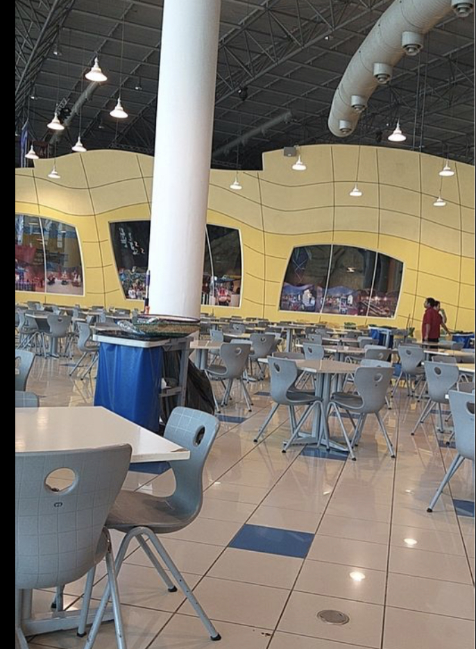 A spacious food court with many tables and chairs, and a distinctive yellow wavy wall.