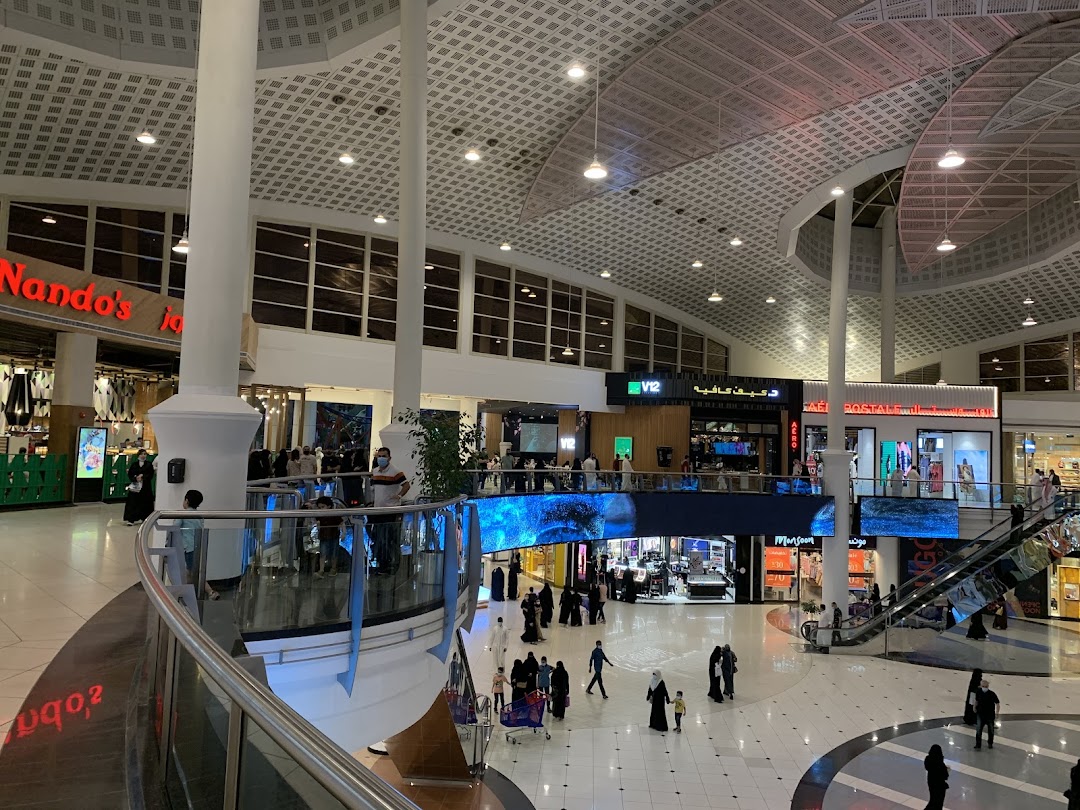 Interior view of a bustling shopping mall with various shops and escalators.