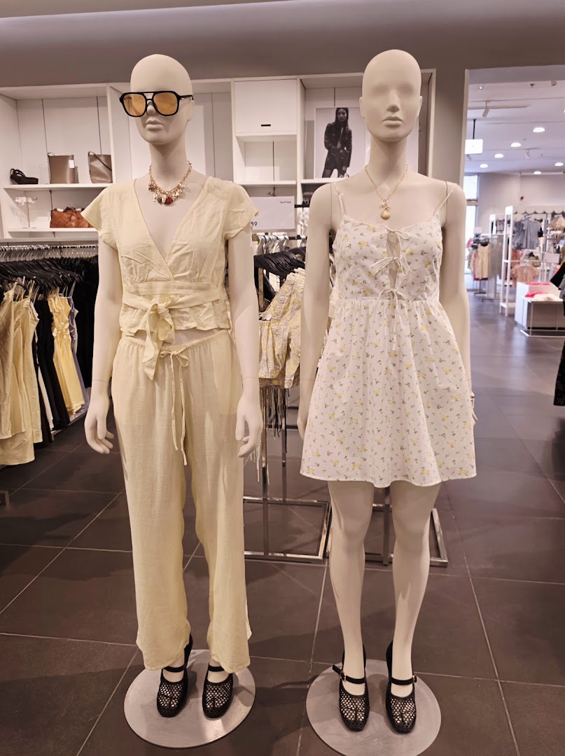 Mannequins display summer outfits with sunglasses and necklaces in a clothing store.