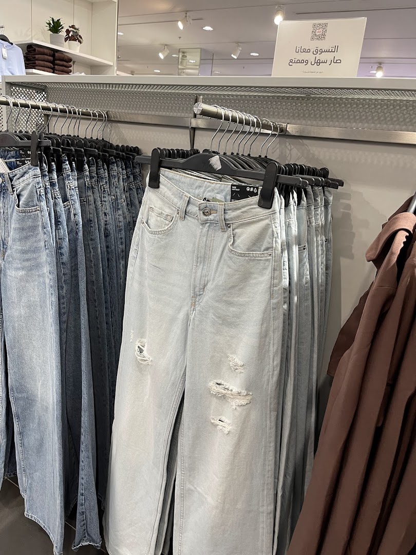 A display of light-wash ripped jeans and other denim clothing on hangers in a retail store.