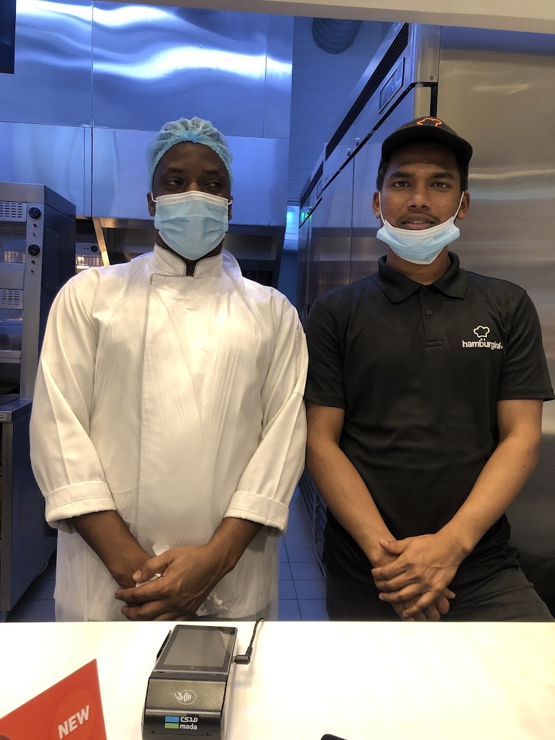 Two staff members, one in a chef's coat and the other in a branded t-shirt, stand behind a counter.