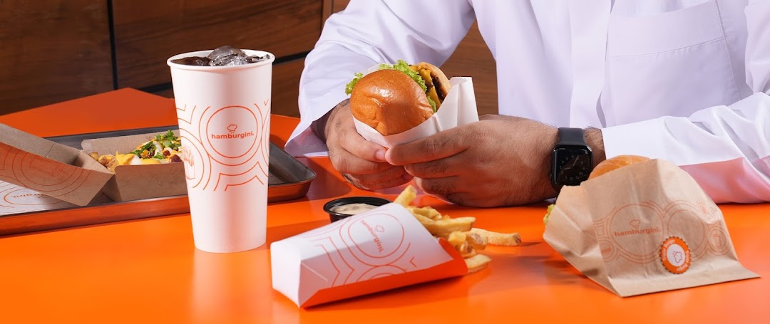 A person enjoys a burger, fries, and drink from Hamburgini.