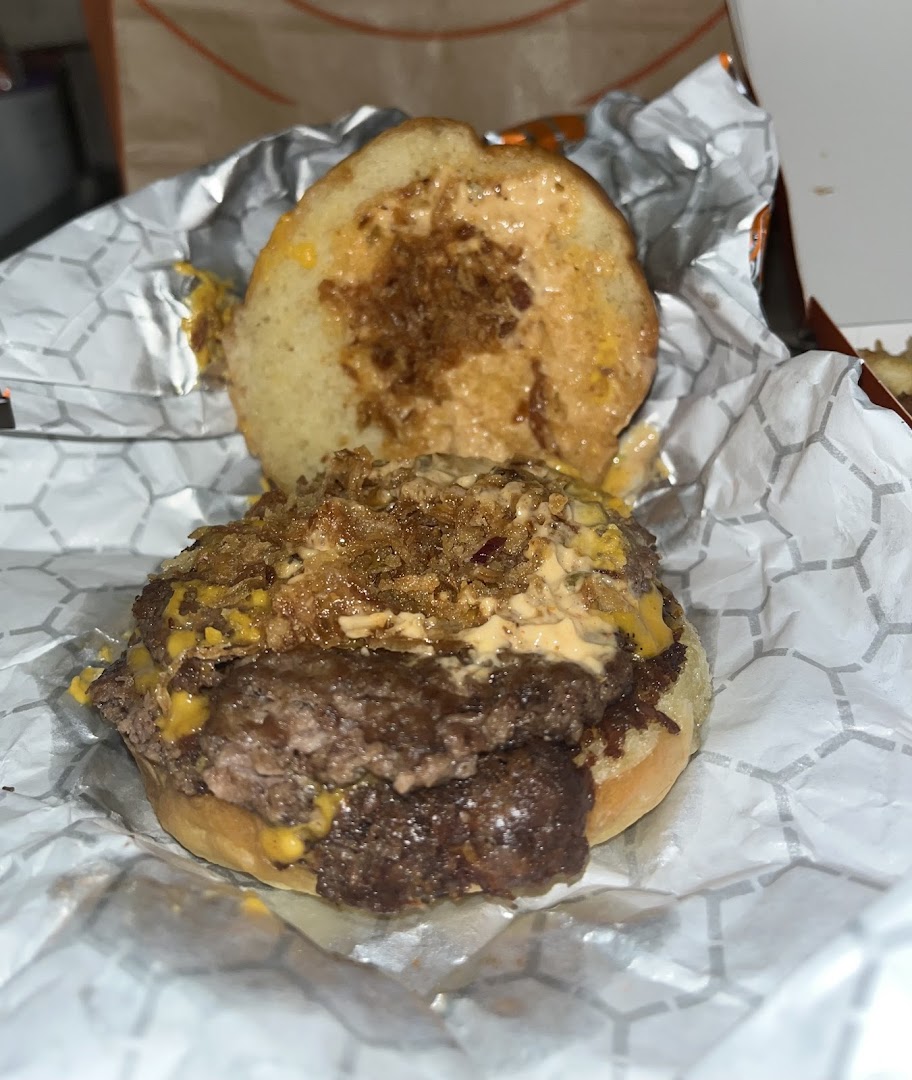 A juicy double-patty burger with crispy onions and sauce, wrapped in paper.