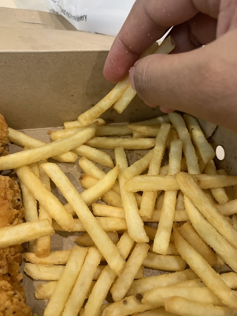 A hand picks up golden french fries from a cardboard box.