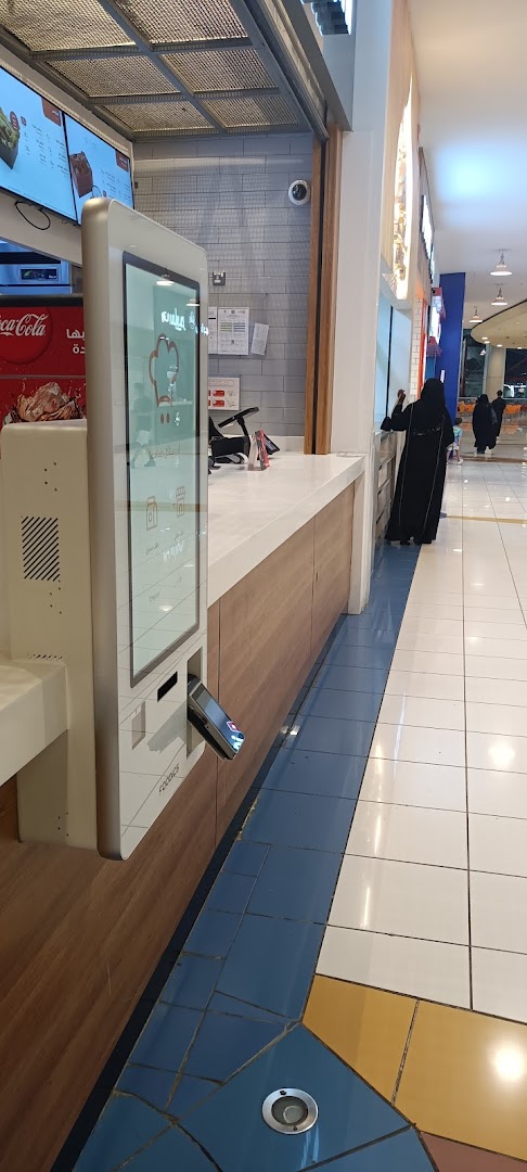 A modern food counter with a digital ordering kiosk and a Coca-Cola display.