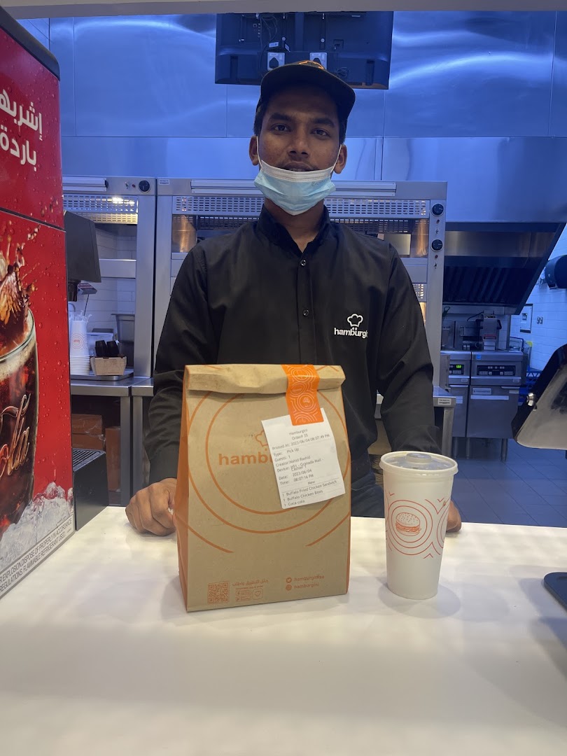 A staff member in a mask stands behind a counter with a takeout bag and drink.