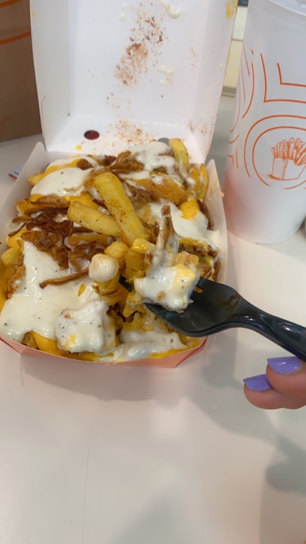 A fork is taking a bite of loaded fries topped with cheese and crispy onions.