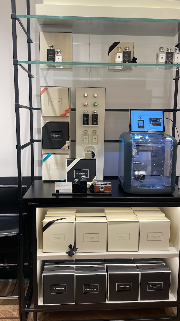 A display shelf showcasing Jo Malone perfumes and gift boxes, with a digital screen and a unique machine.
