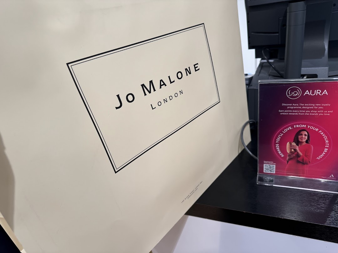 A Jo Malone shopping bag and a sign for the Aura loyalty program.