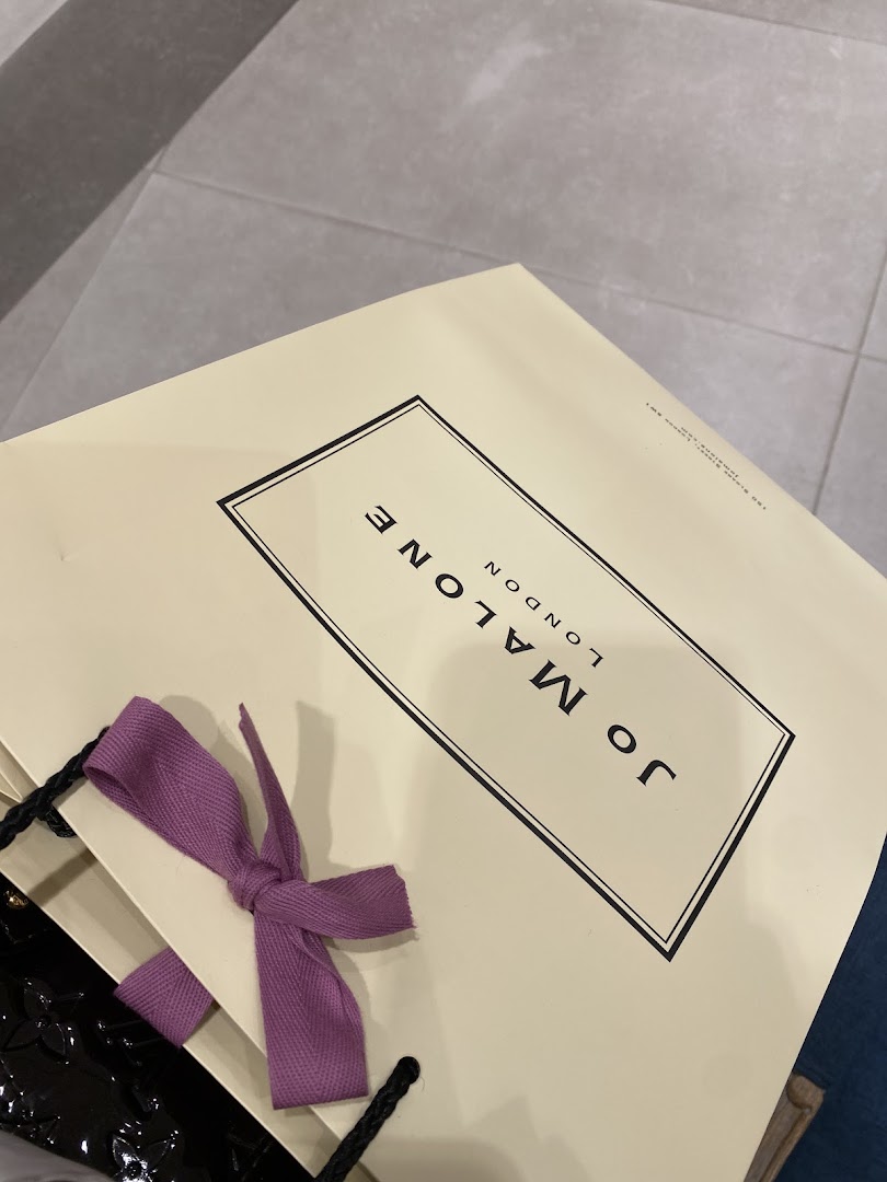 A Jo Malone shopping bag with a purple ribbon and a black glossy item.