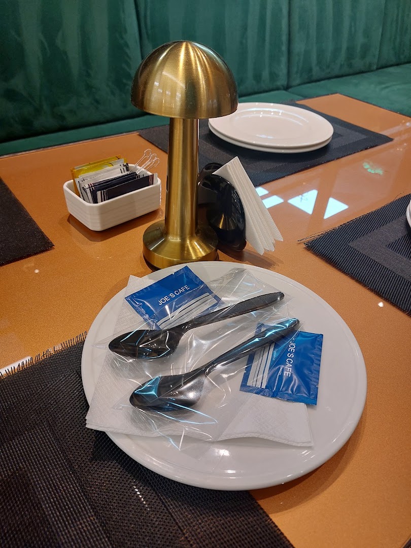 A table setting at Joe's Cafe with plates, cutlery, a lamp, and sugar packets.