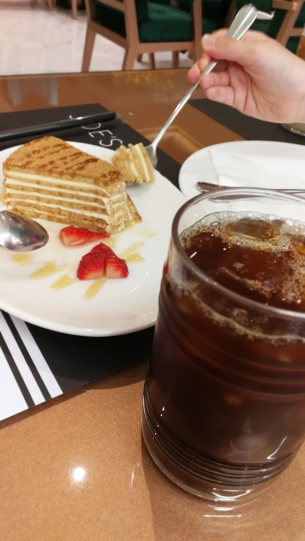 A slice of layered cake with strawberries and a glass of iced coffee.