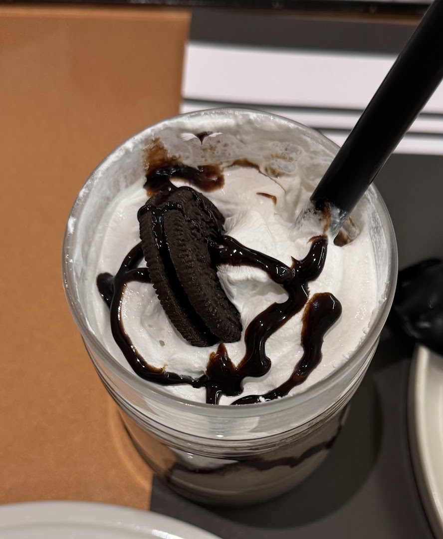 A close-up of an Oreo milkshake topped with whipped cream and chocolate syrup.
