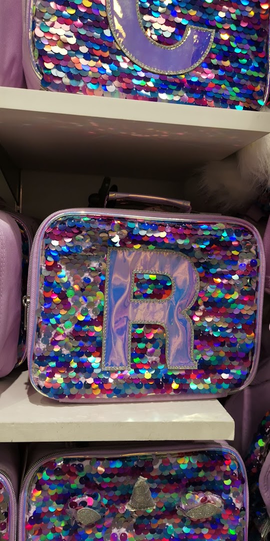 Close-up of sequined lunch bags with letters 'R' and 'G' on shelves.