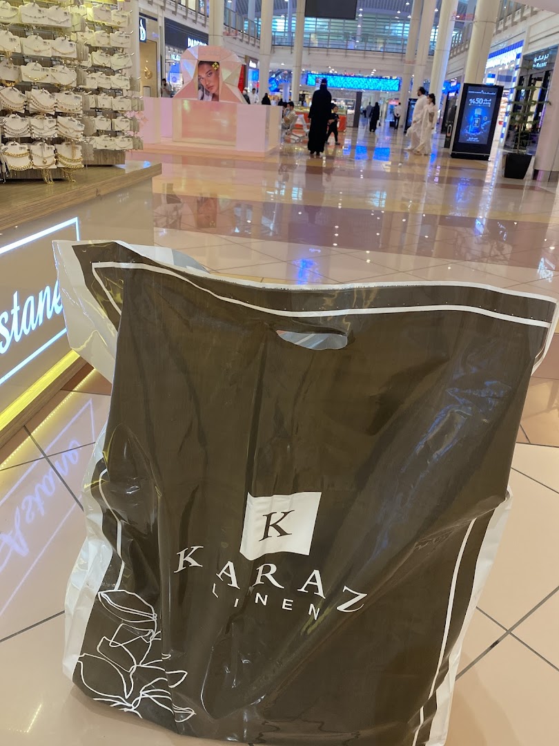 A shopping bag from Karaz Linen in a brightly lit mall with other shops visible.
