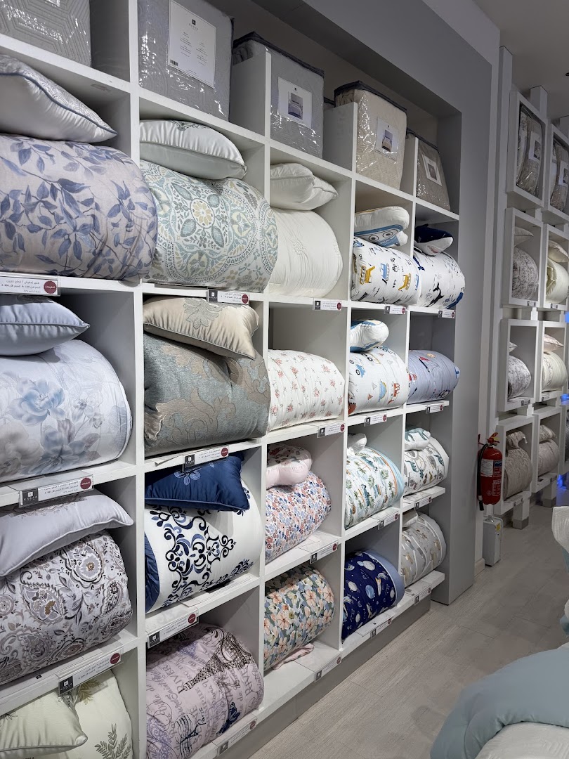 A retail shop interior displaying a wide variety of bedding and linens on shelves.