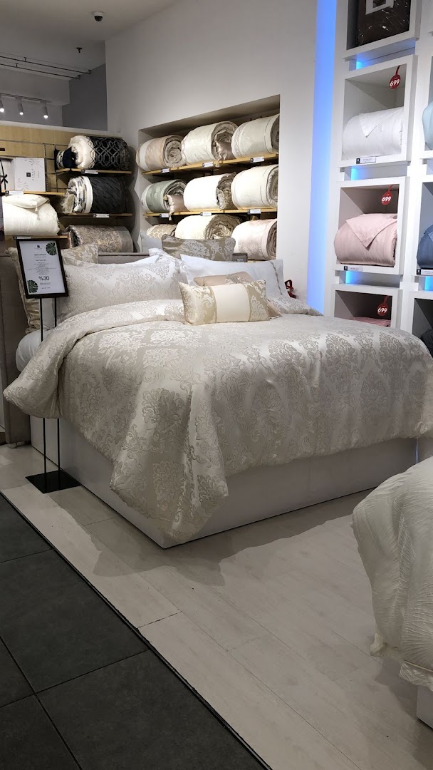 A beautifully made bed with elegant white bedding and decorative pillows, surrounded by rolled linens.