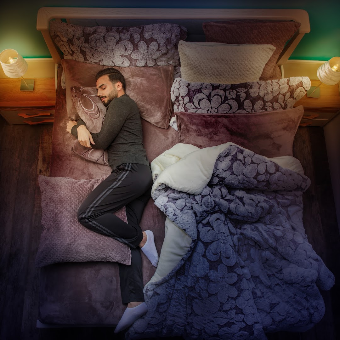 A man sleeps peacefully in a luxurious bed with plush pillows and a patterned duvet.
