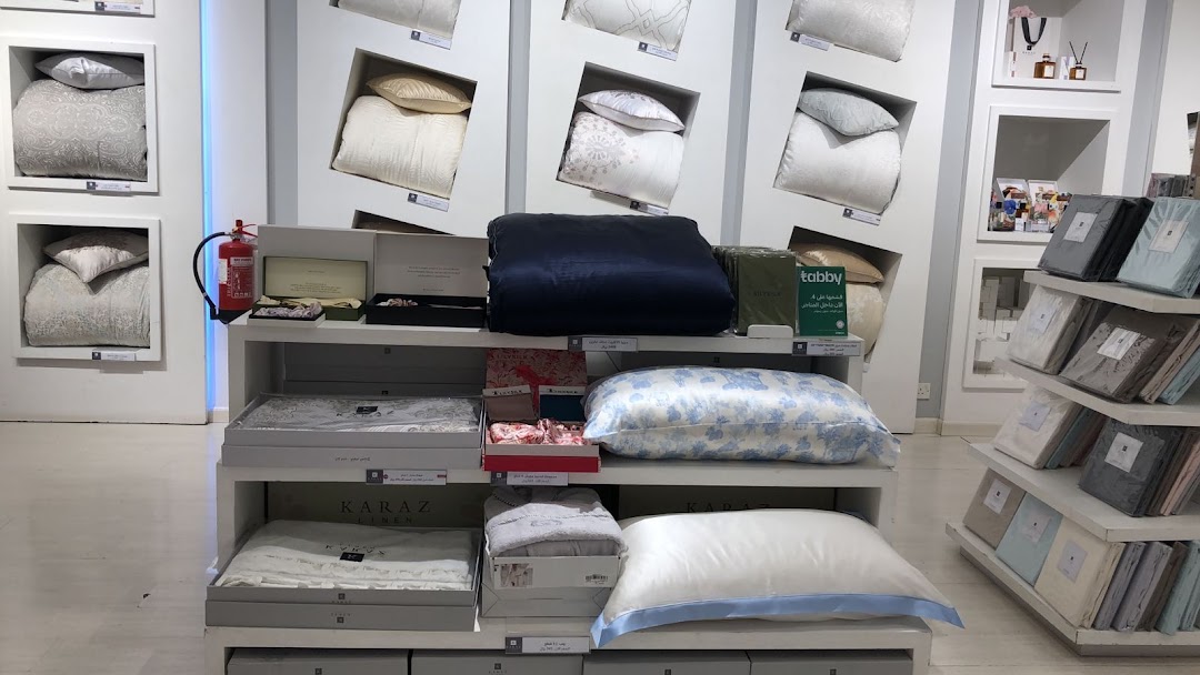Karaz Linen shop interior displaying various bedding sets, pillows, and folded linens on shelves.