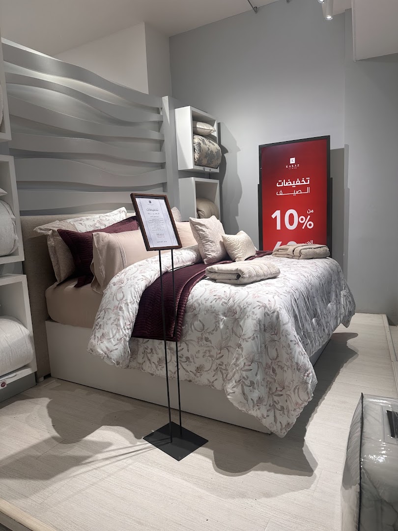 A beautifully made bed with floral bedding and a burgundy throw, displayed in a store with a sale sign.