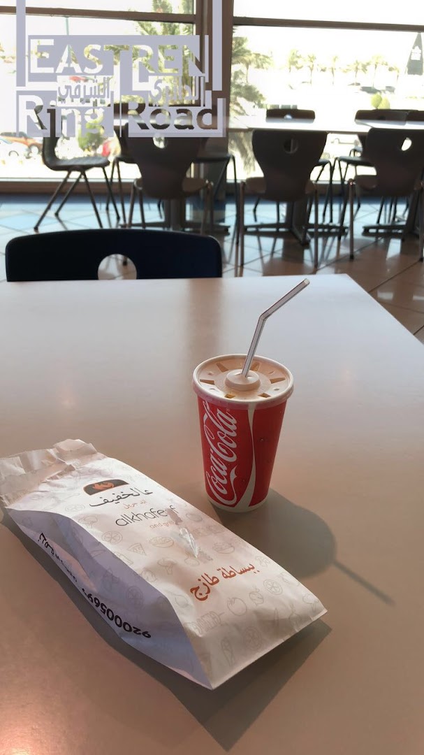 A Coca-Cola drink and a paper bag from Alkhofef restaurant on a table.