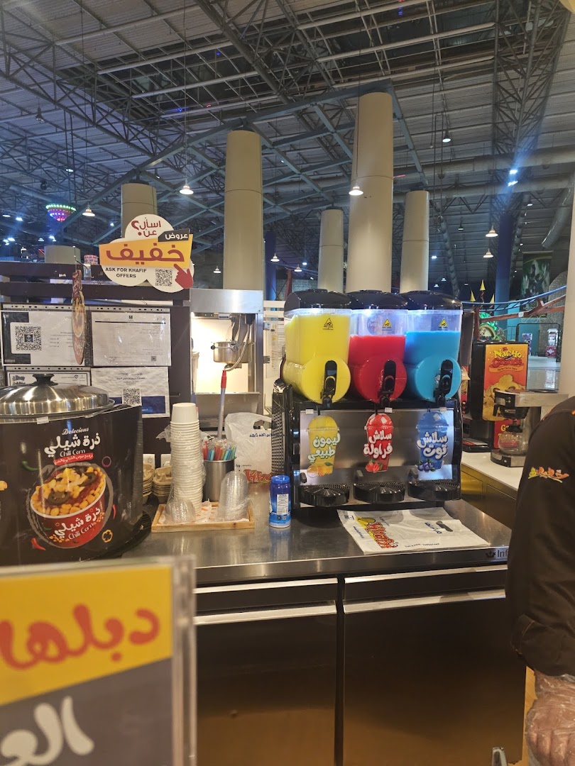 A food counter with a slush machine, chili corn dispenser, and various signage.