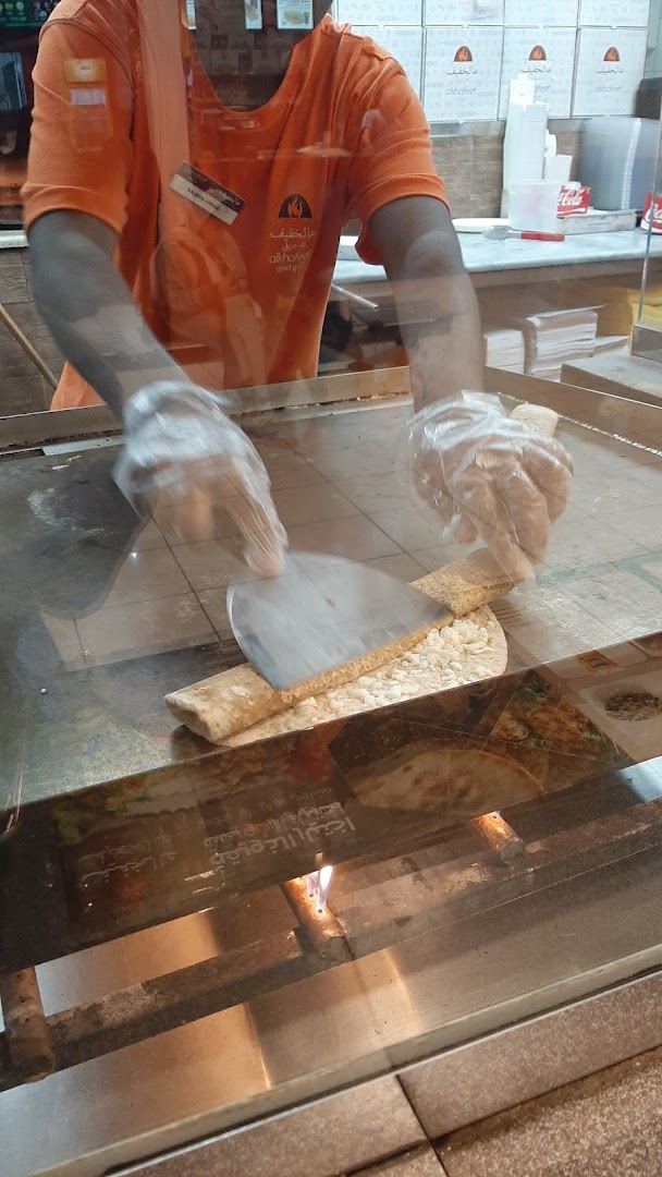 A chef in an orange uniform prepares food on a grill, with the shop's logo visible.