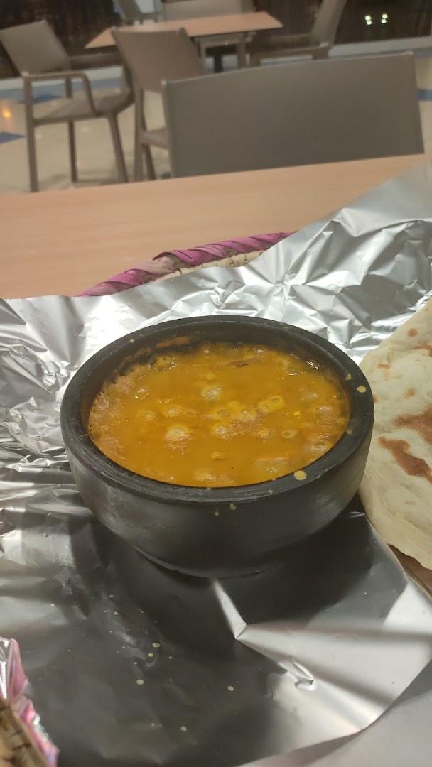 A close-up of a hearty stew served in a black bowl with flatbread on the side.