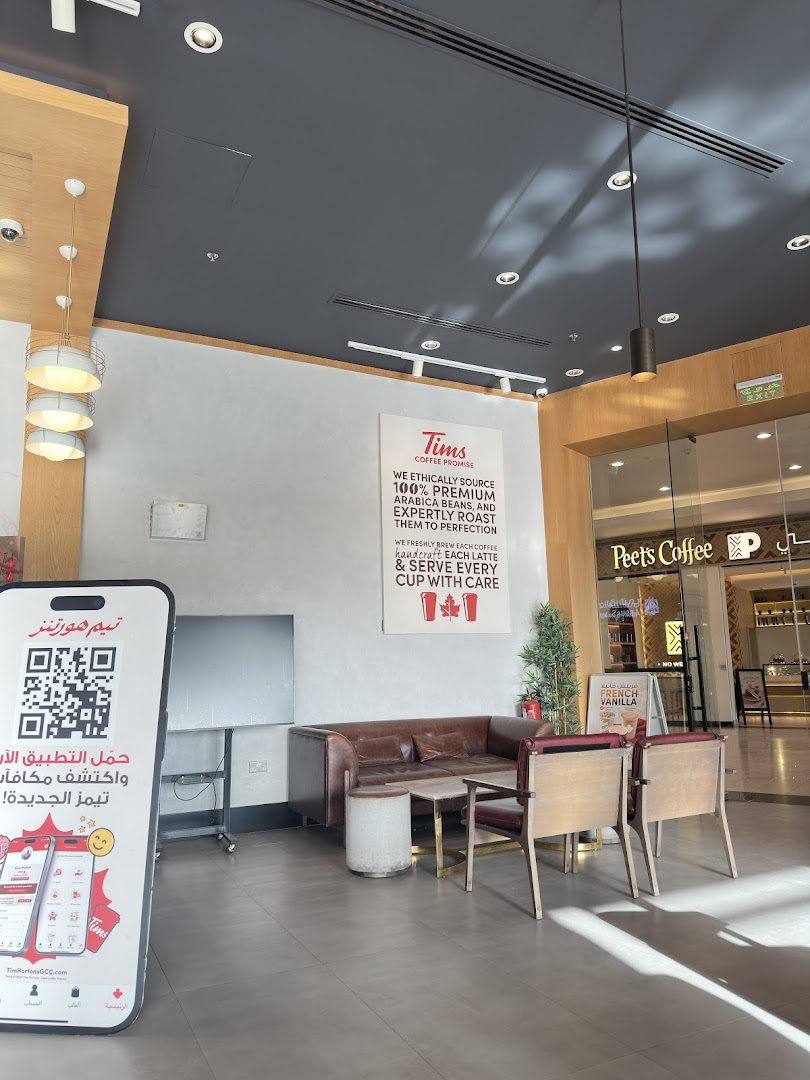 Interior seating area of a coffee shop with a large promotional stand and a sign detailing the coffee promise.