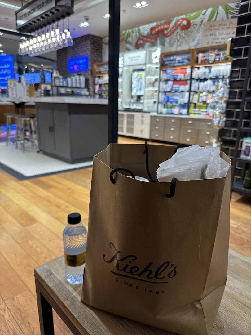 A Kiehl's shopping bag and water bottle sit on a wooden table in front of the store.