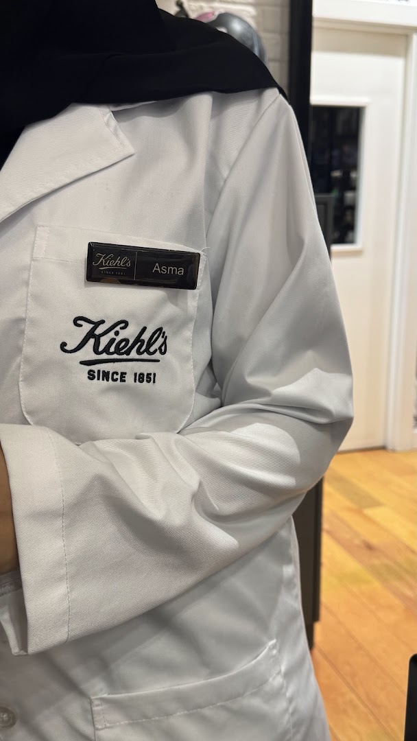 A person wearing a white Kiehl's lab coat with a name tag.