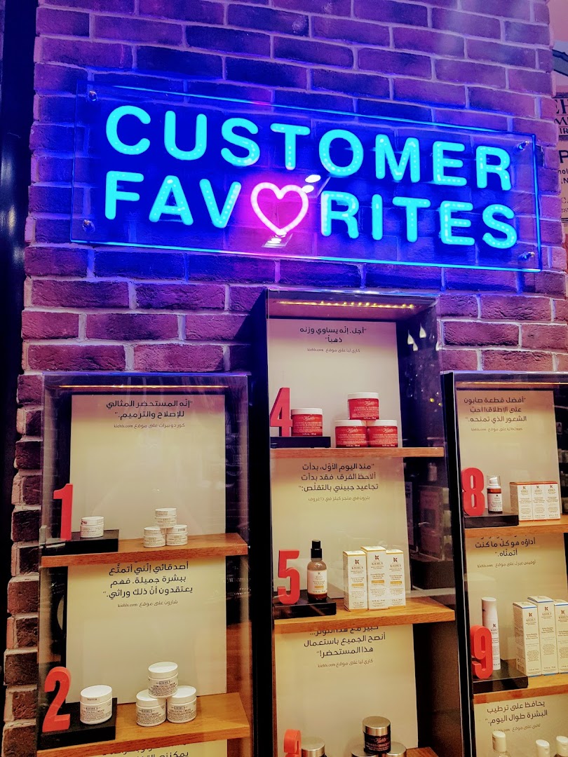 A neon sign reading 'CUSTOMER FAVORITES' above shelves displaying Kiehl's skincare products.