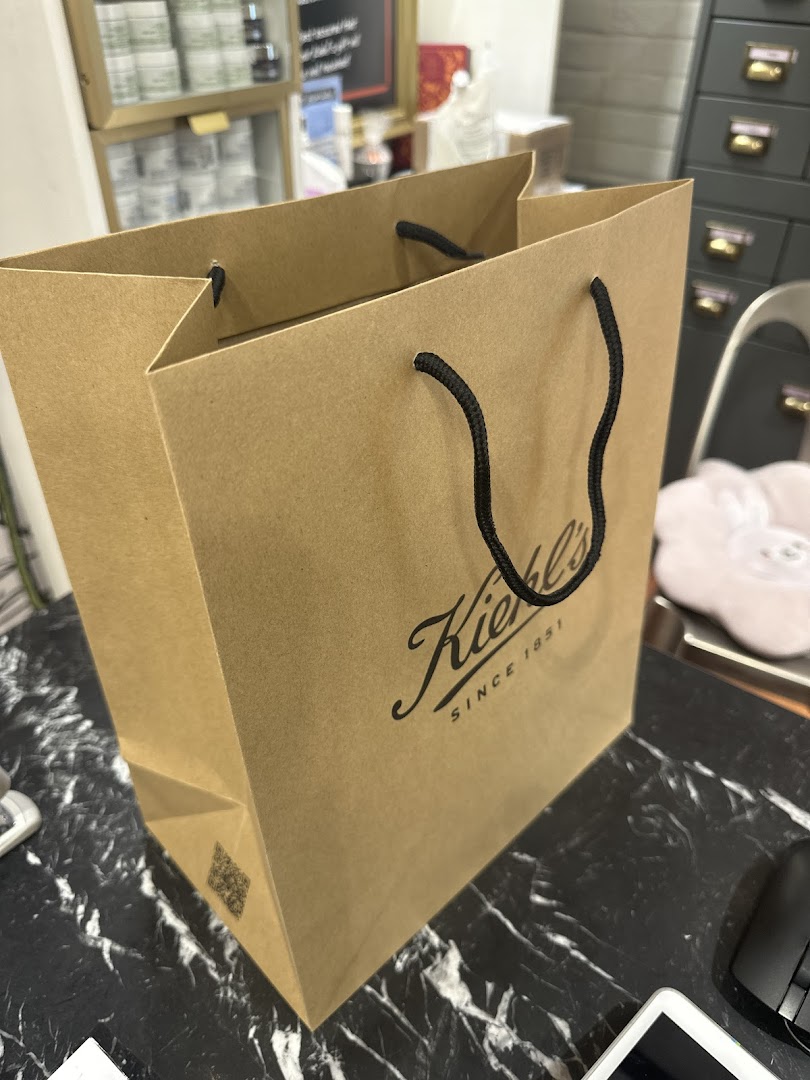 A Kiehl's shopping bag with black handles sits on a black and white marble surface.
