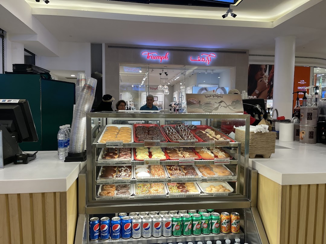 A display case filled with various donuts and cans of soda at a Krispy Kreme shop.