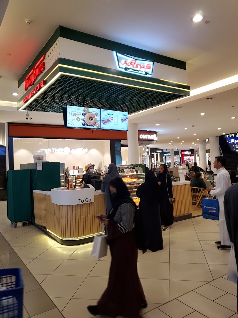 Krispy Kreme donut shop counter with customers and a digital menu board.