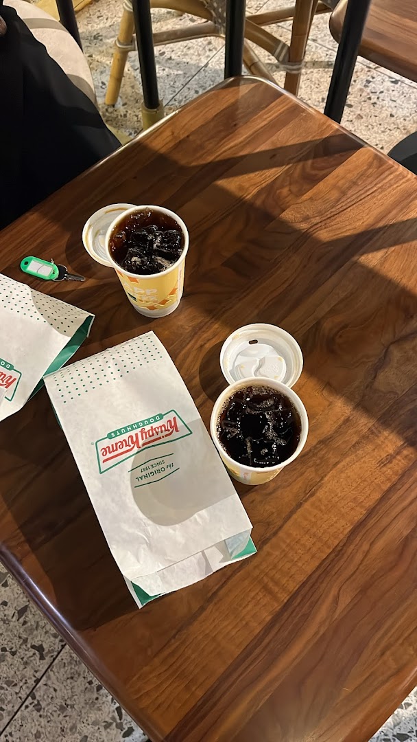Two cups of iced coffee and Krispy Kreme bags on a wooden table.