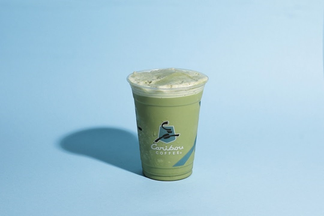 A refreshing green iced beverage with foam on top, branded with Caribou Coffee logo.