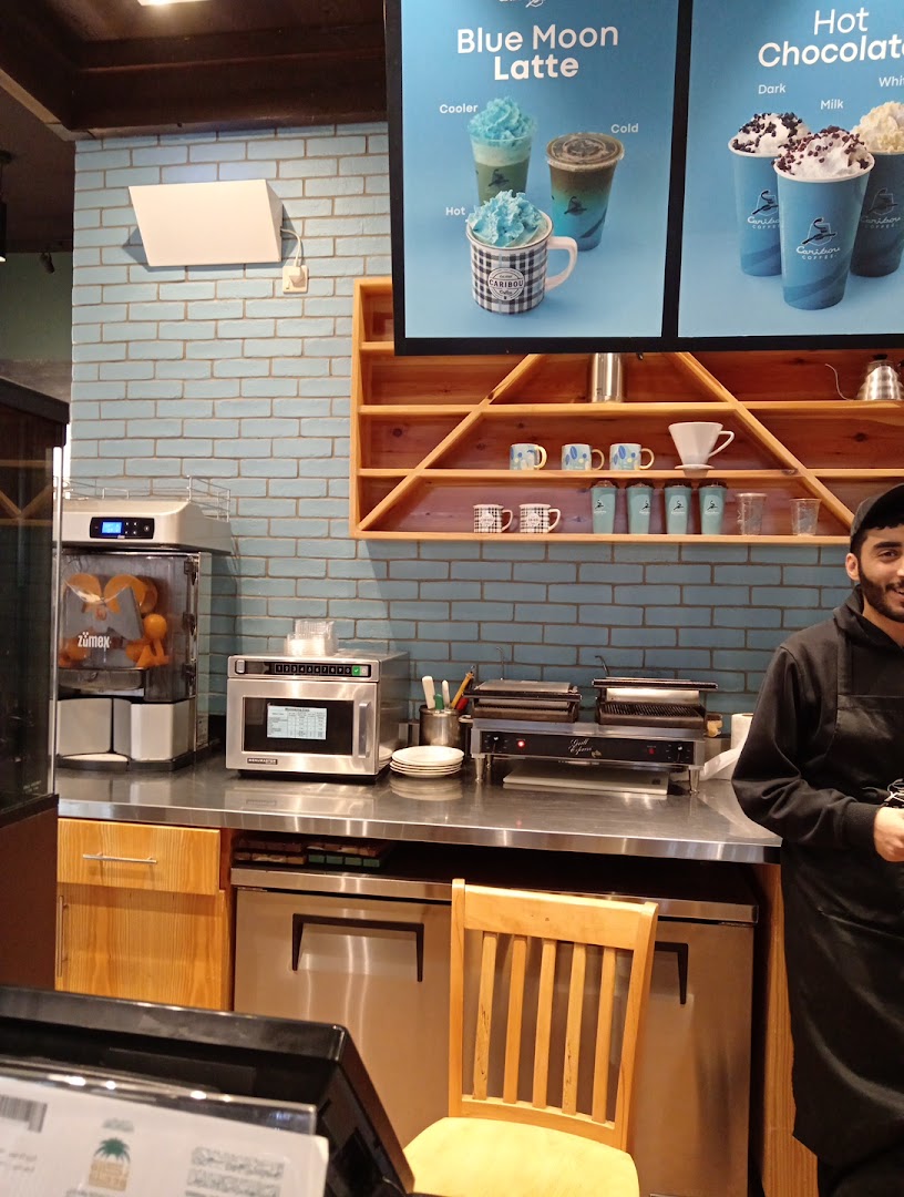 Caribou Coffee counter with drinks display, equipment, and a staff member.