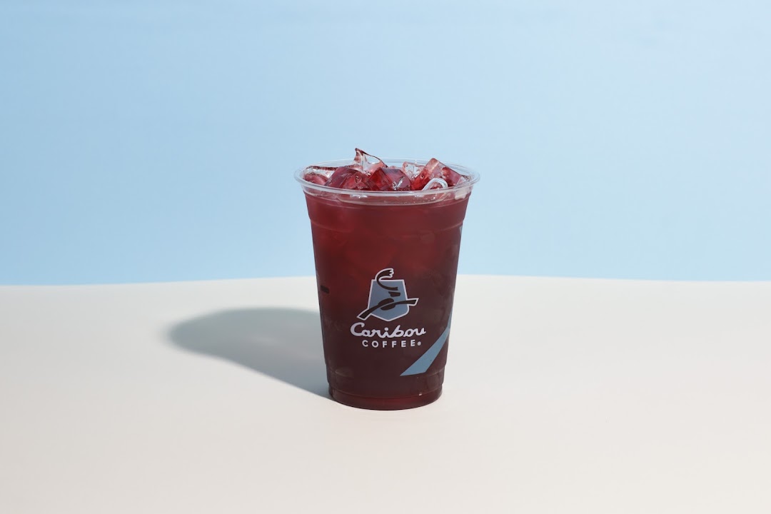 A refreshing iced beverage with a deep red color and ice cubes in a clear plastic cup.