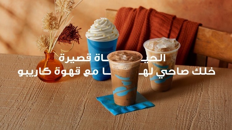 Three iced coffee drinks from Caribou Coffee on a wooden table with decorative dried plants.